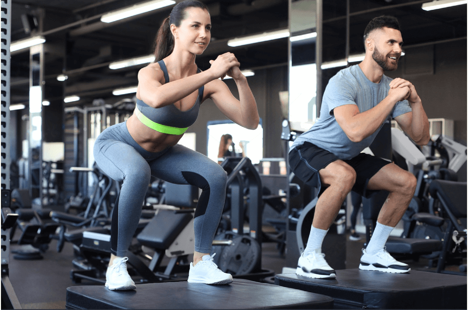 Fit couple doing jumping squats in crossfit gym