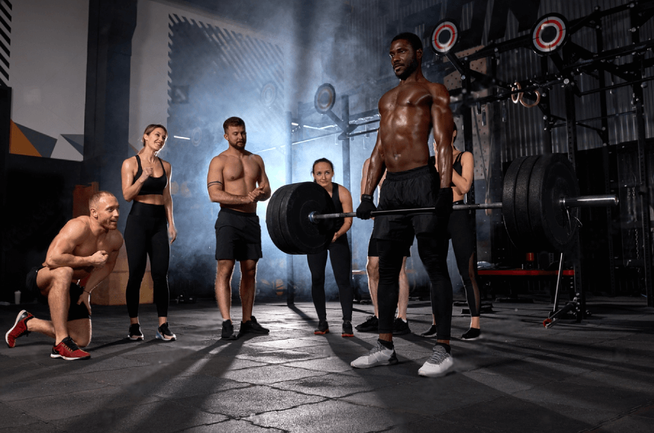 Fit young african black man lifting barbells looking focused working out in gym with other people looking at him supporting at competition. Sport cross fit bodybuilding concept