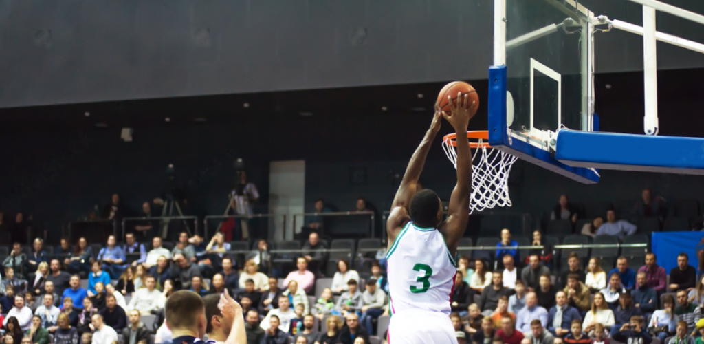 basketball player throws a ball into the hoop in the background the fans are sitting