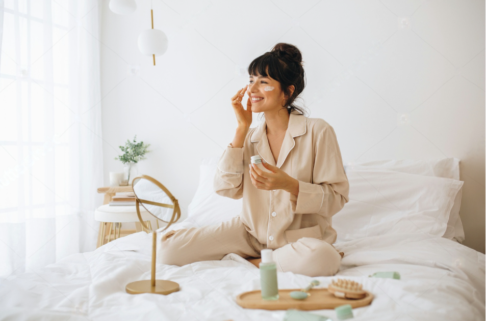 happy woman doing routine skin care at home with beauty products woman sitting on bed at home