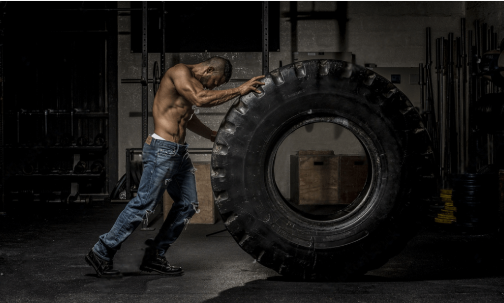 muscular man in jeans holding large tire